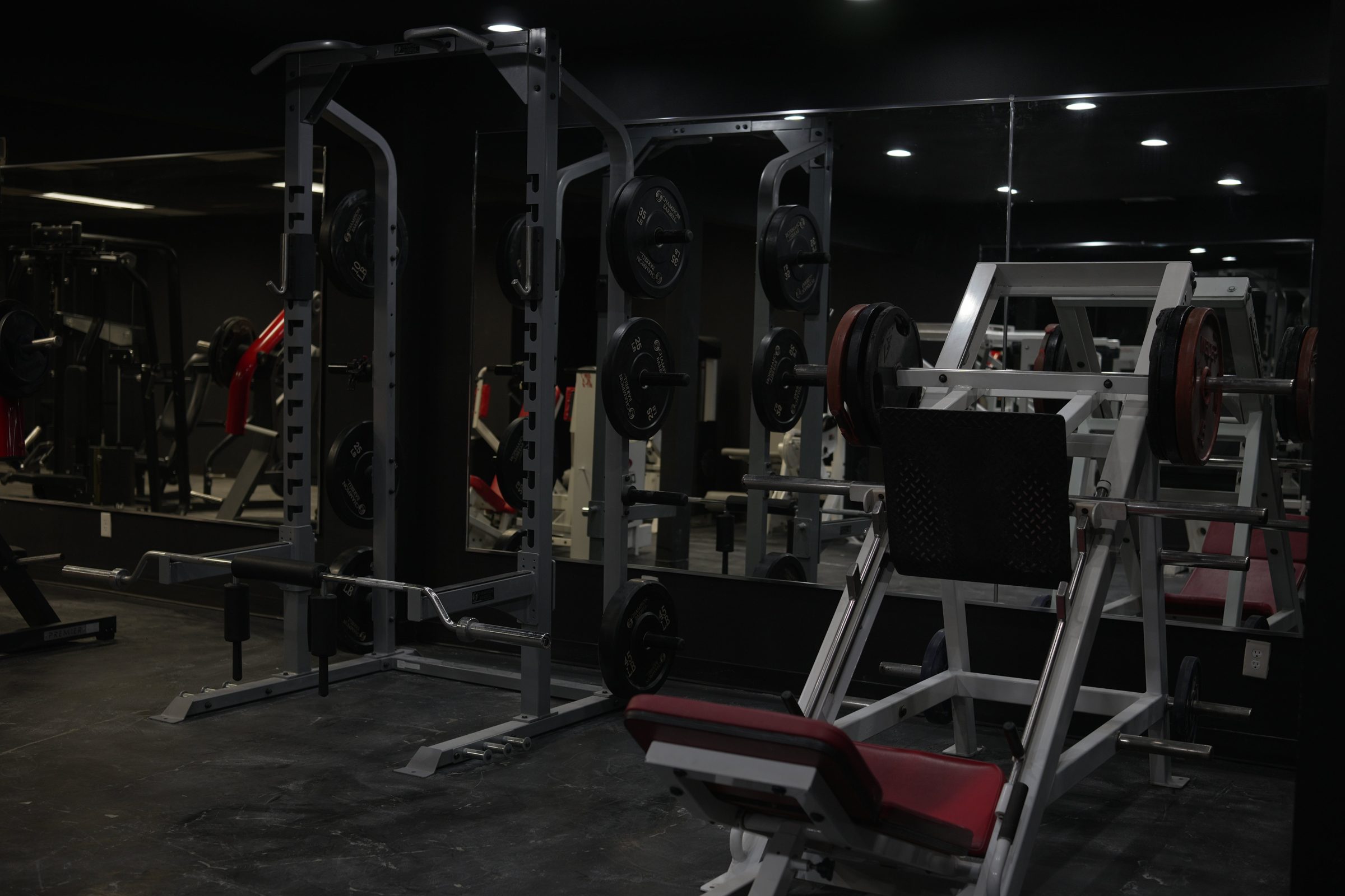 Two power racks with plates next to a red-padded leg press