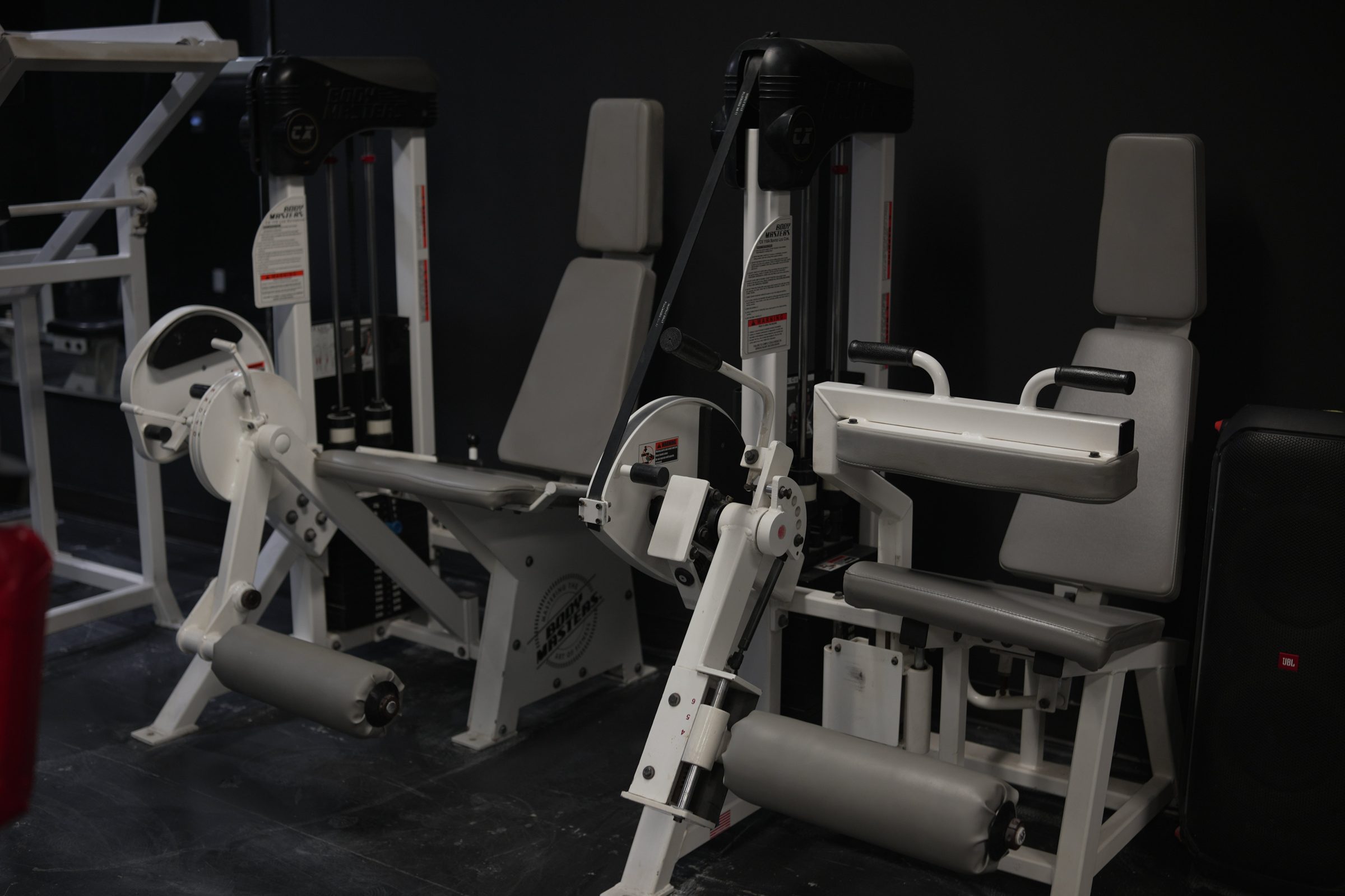 Two classic white leg-extension machines against a black wall